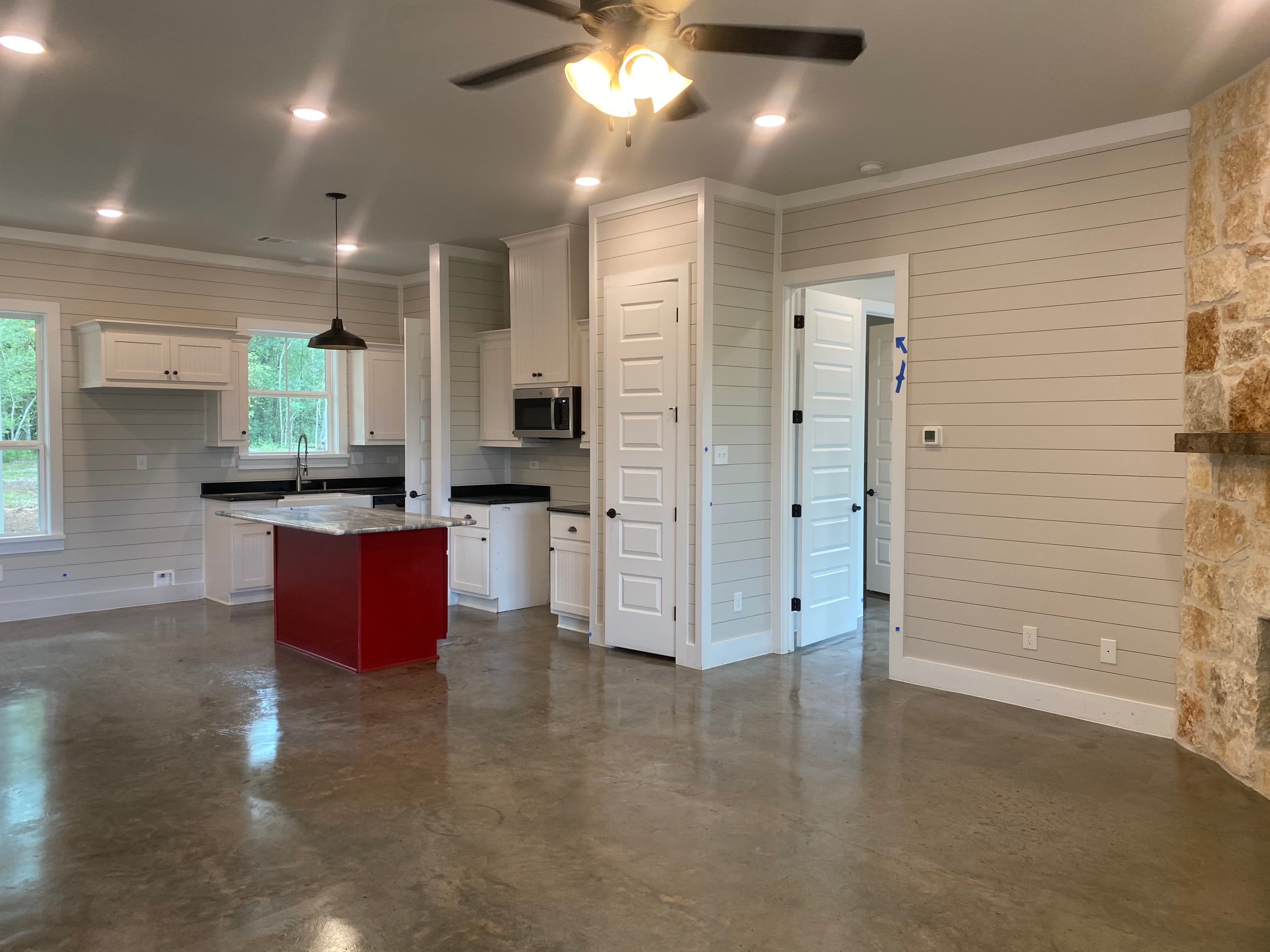 Modern kitchen with red island, white cabinets, shiplap walls, stone fireplace, and polished concrete floors.