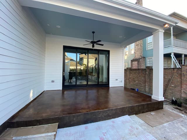 Covered patio featuring dark stained concrete floors, a light blue ceiling, and black sliding doors.