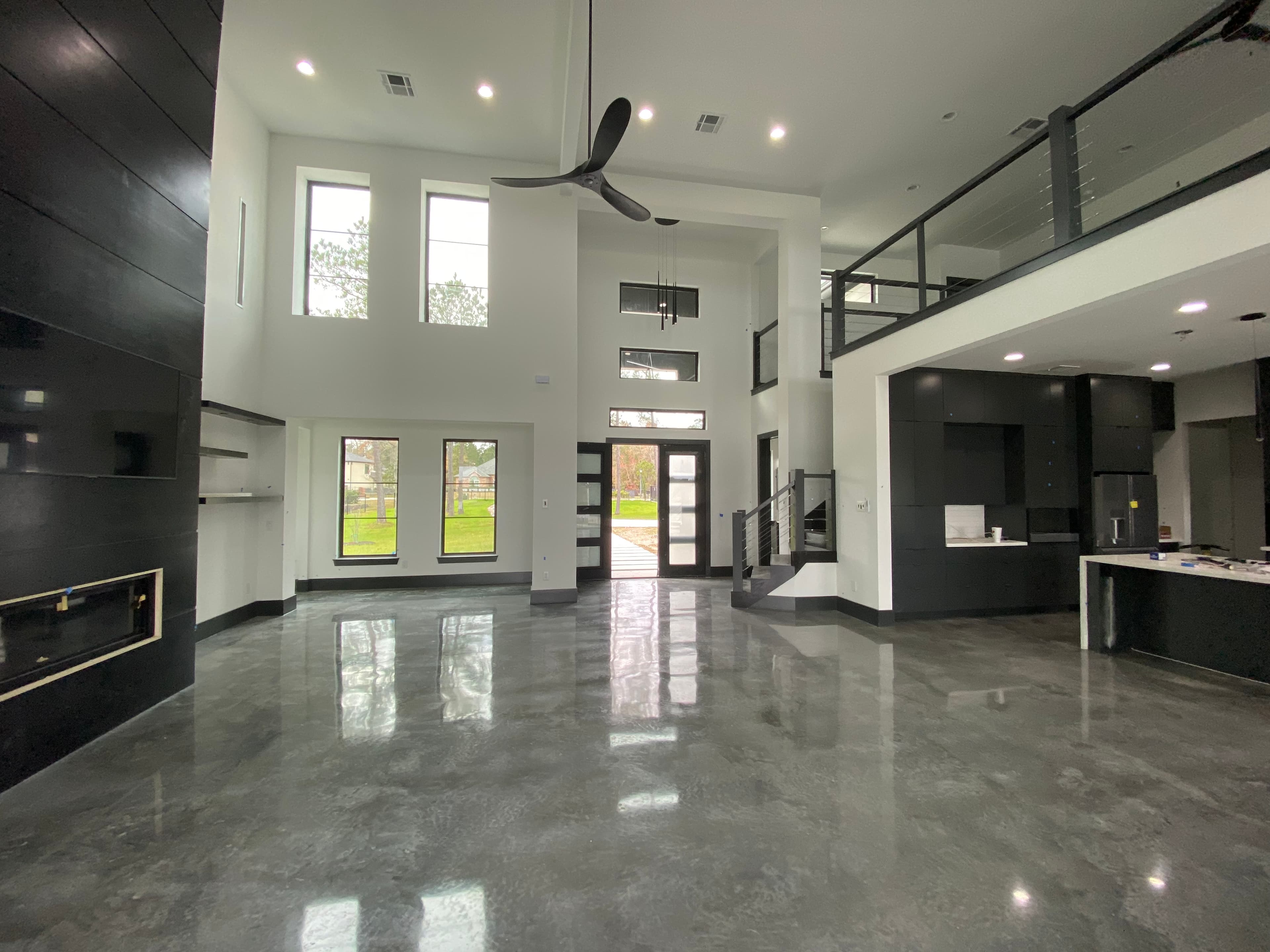 Modern open-concept home featuring polished concrete floors, high ceilings, black accents, and large windows.