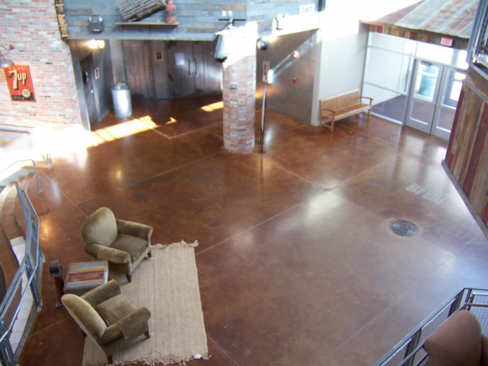 Elevated view of an industrial lobby with polished brown floors, green armchairs, and brick pillars.