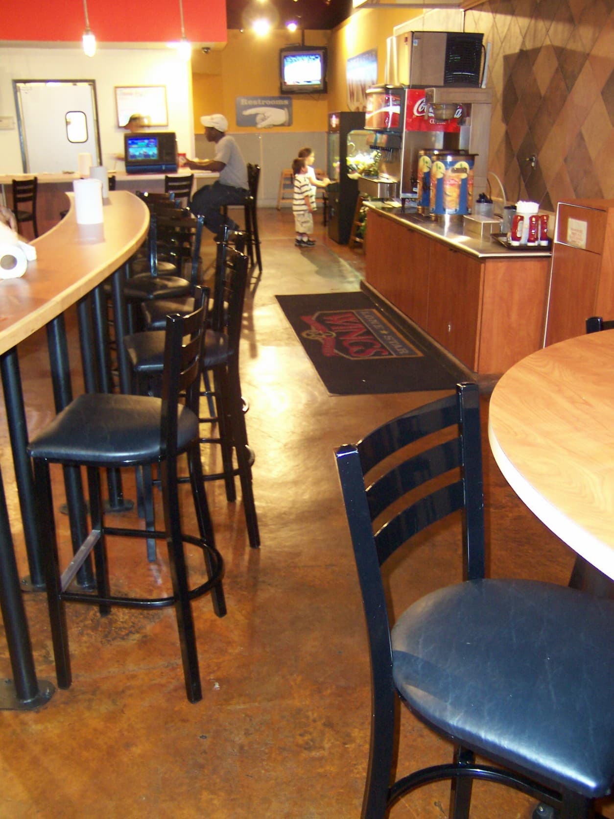 Restaurant interior with a curved wooden bar, black stools, and a soda fountain station.
