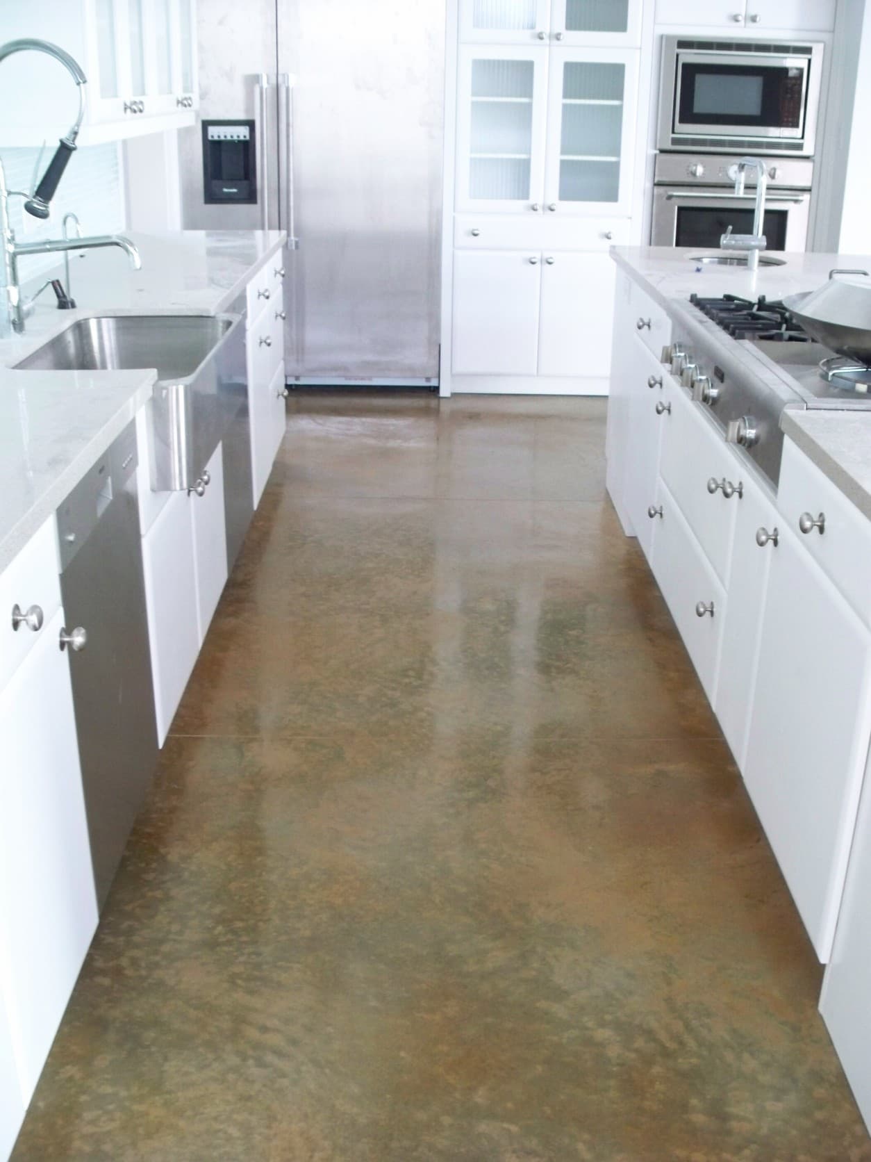 Polished brown stained concrete floor between white kitchen cabinets and stainless steel appliances.