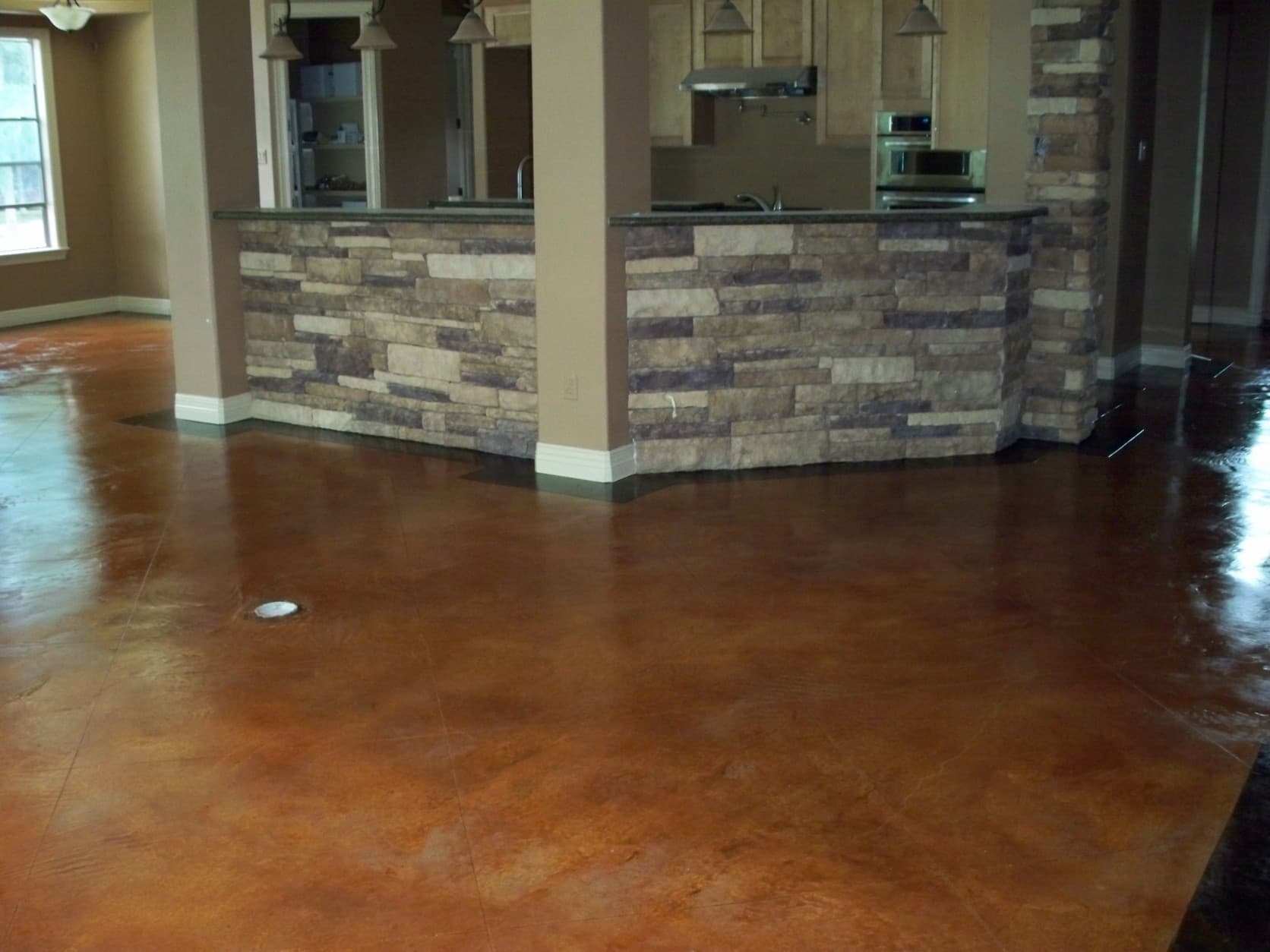 Polished reddish-brown stained concrete floor in a room with a stone-faced kitchen counter.