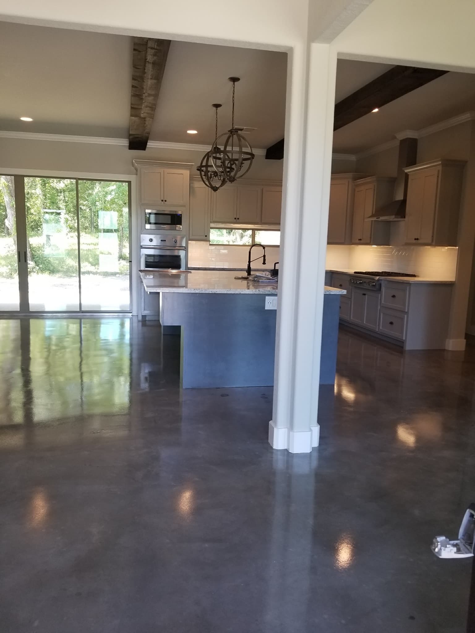 Modern kitchen with polished concrete floors, blue island, white cabinets, and wooden ceiling beams.